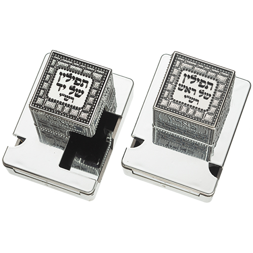 זוג בתי תפילין מפלסטיק בעיצוב מוקפד עם פלקטה, האחד פתוח חלקית וחושף פנים שחור, במבט עילי זוויתי.