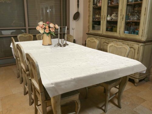 מפת שולחן מלבנית מעוטרת בדוגמה עדינה פרוסה על שולחן אוכל חגיגי מוקף כיסאות בחדר אוכל בסגנון כפרי